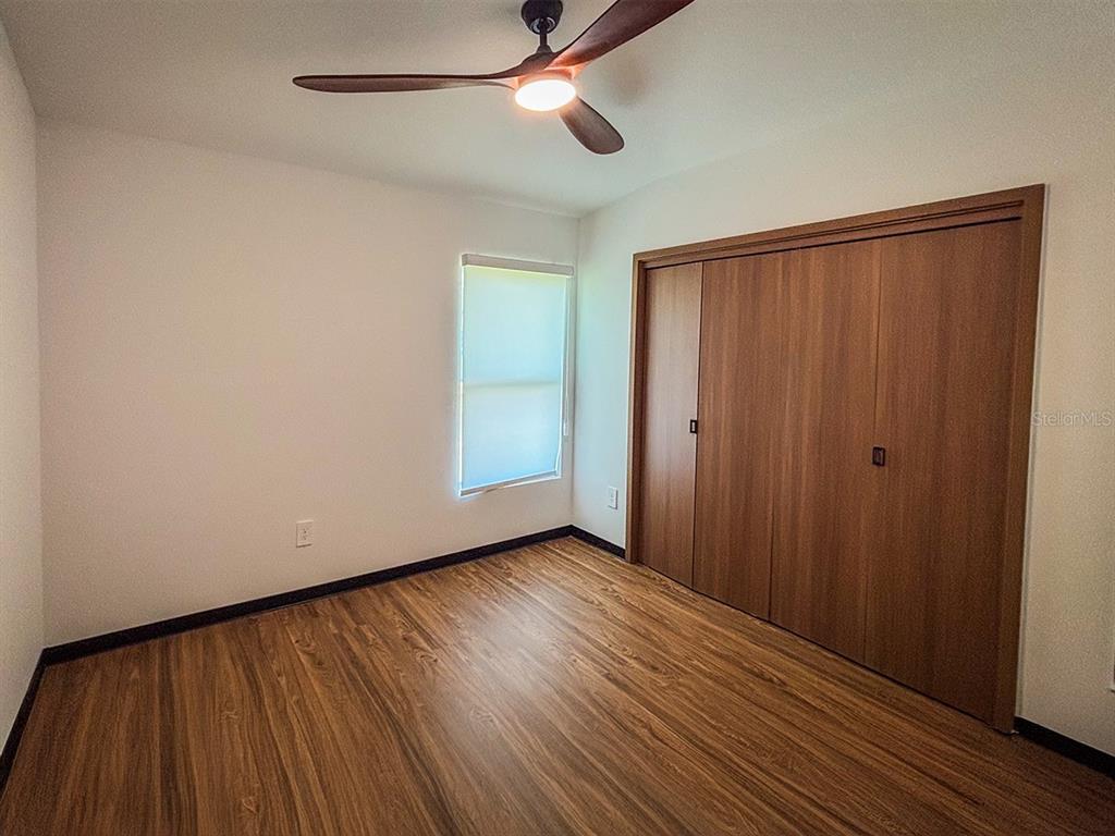 A bedroom with wood-look flooring, a ceiling fan, a window, and a wooden closet — 5830 VIRTUDES STREET, SEBRING, FL