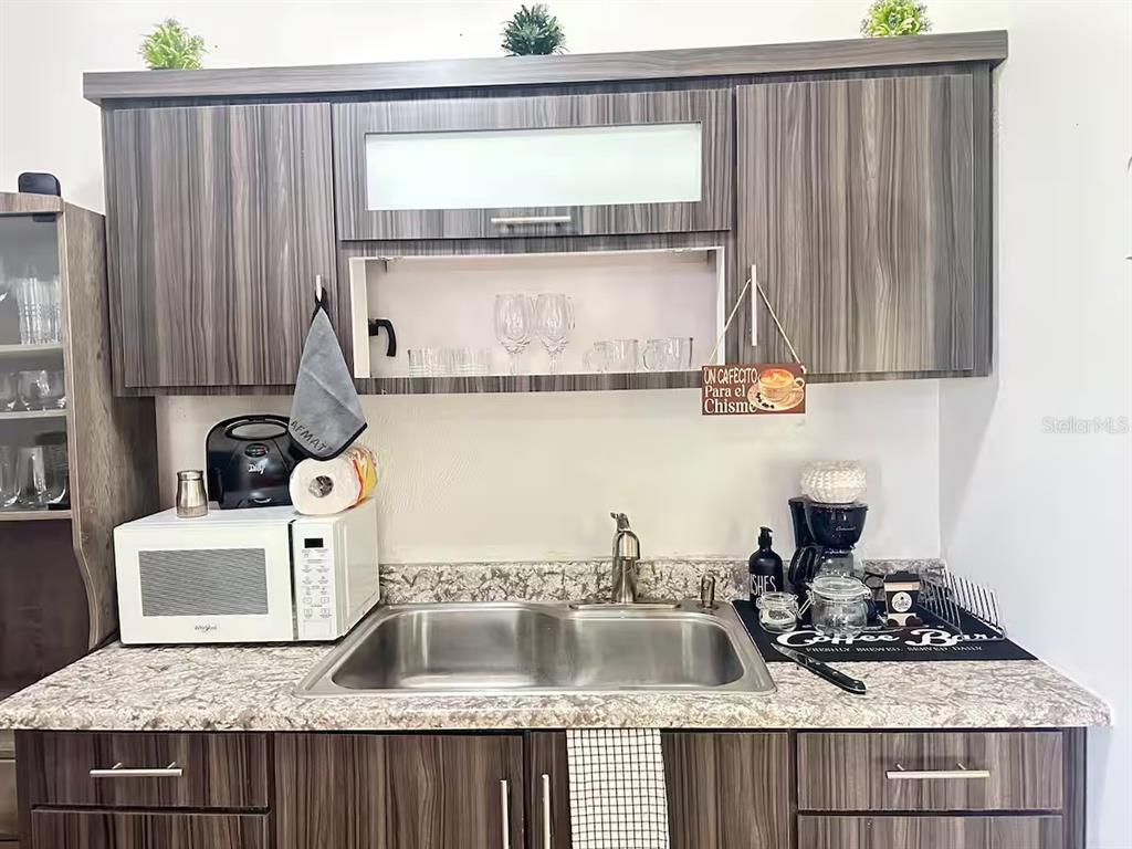 A kitchen features wood-grain cabinets, a double-basin stainless steel sink, and a white microwave — Aguas Buenas 5.9 795 SECTOR GARAY, AGUAS BUENAS, PR