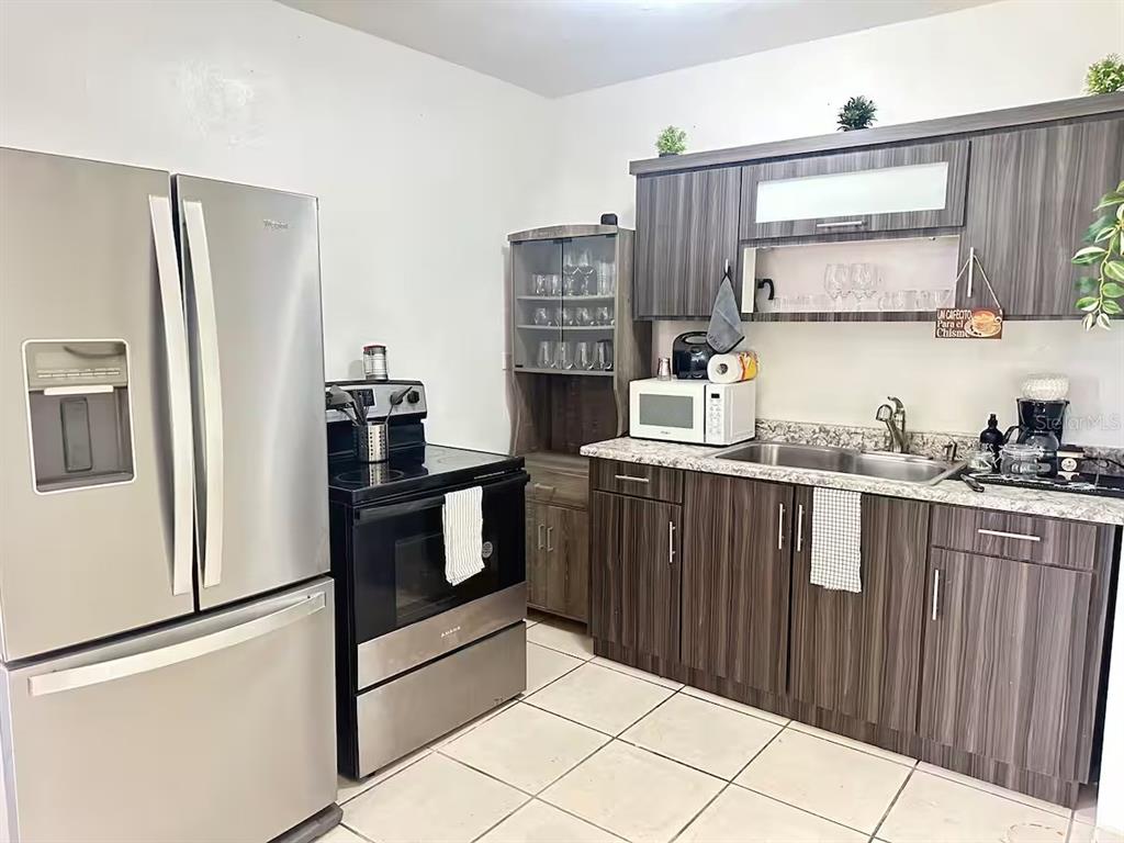 A kitchen features stainless steel appliances, dark wood-grain cabinets, and light-colored tile flooring — Aguas Buenas 5.9 795 SECTOR GARAY, AGUAS BUENAS, PR