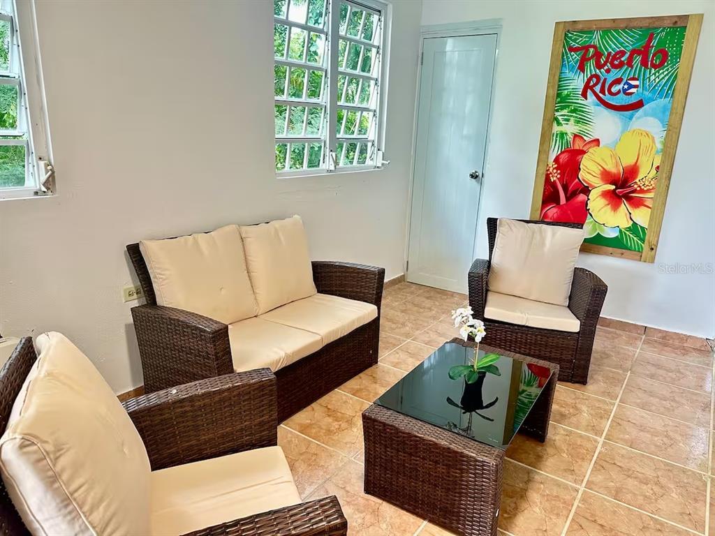 A living room features wicker furniture, a glass coffee table, and a Puerto Rico wall sign — Aguas Buenas 5.9 795 SECTOR GARAY, AGUAS BUENAS, PR