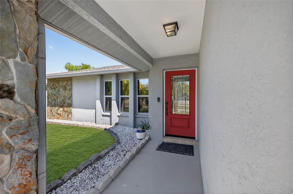 A covered entryway features a bright red front door, light gray walls, and stone accents — 10275 113TH STREET, SEMINOLE, FL