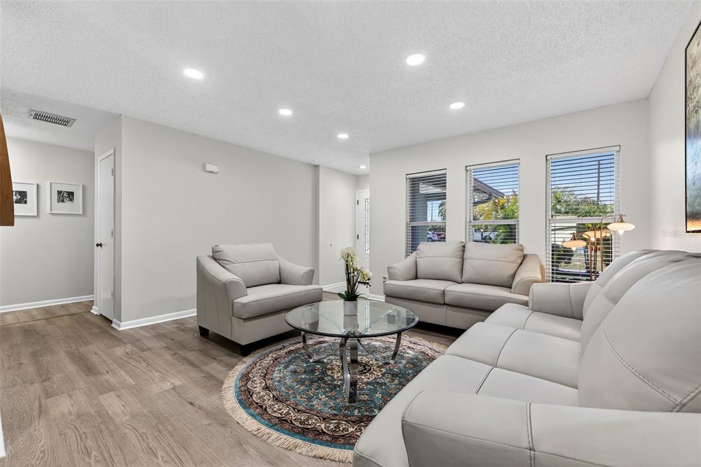A living room features light gray walls, wood-look flooring, and a white leather furniture set — 10275 113TH STREET, SEMINOLE, FL