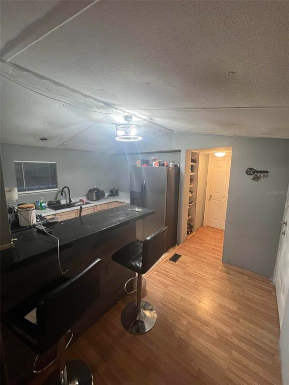 A kitchen features a black breakfast bar, stainless steel refrigerator, and light wood-look flooring — 10809 SE 129TH STREET, BELLEVIEW, FL