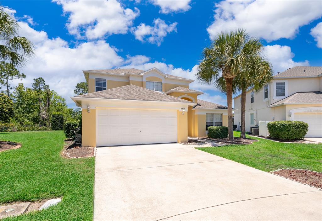 A two-story yellow house features a two-car garage, a concrete driveway, and palm trees — 2808 LIDO KEY COURT, KISSIMMEE, FL