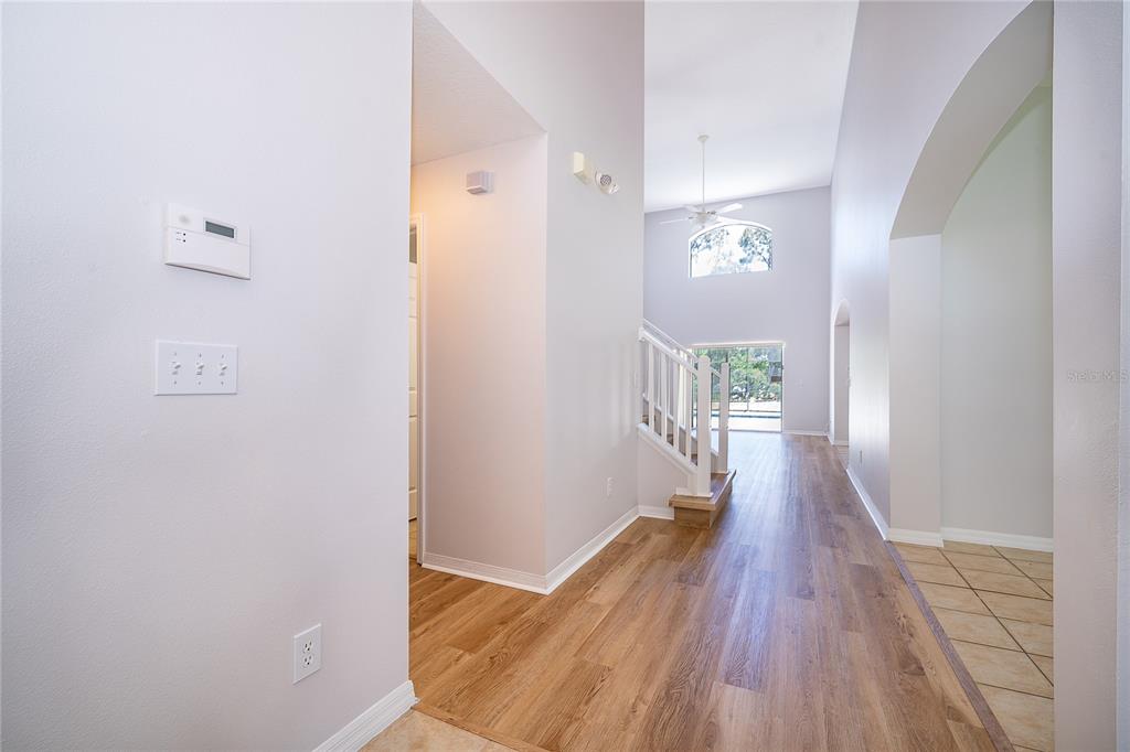 A bright entryway with wood-look flooring leads to a staircase and a high-ceilinged living area — 2808 LIDO KEY COURT, KISSIMMEE, FL