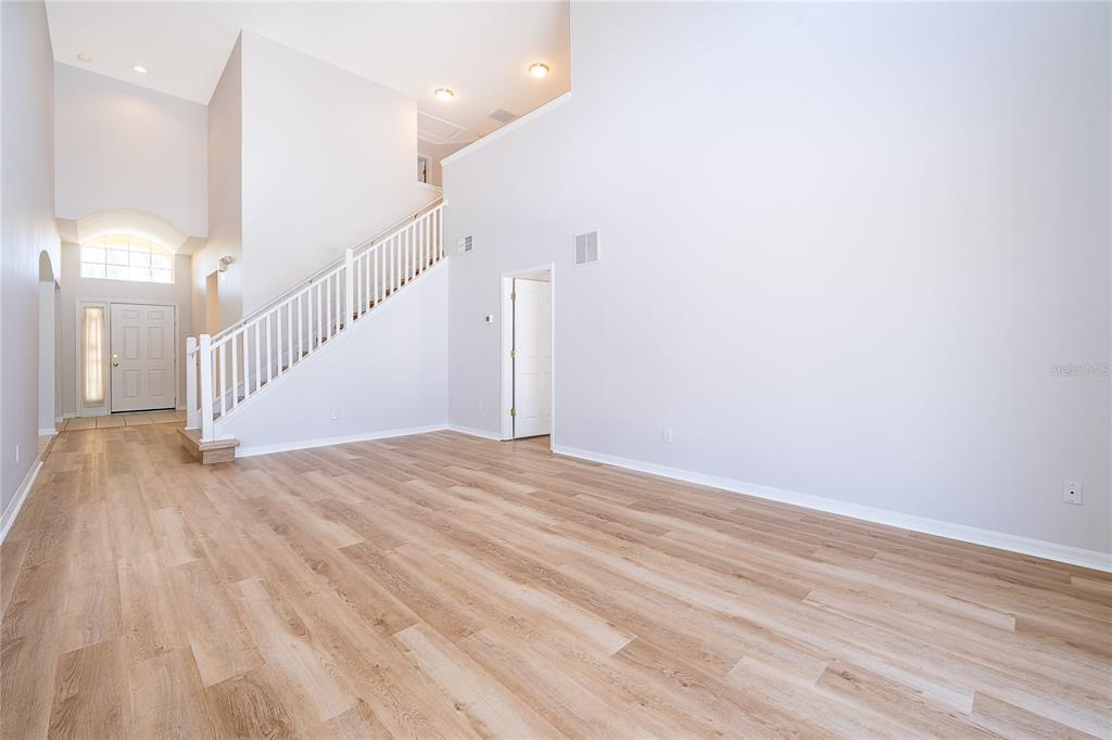An empty living room features light wood-look flooring, high ceilings, and a staircase with railings — 2808 LIDO KEY COURT, KISSIMMEE, FL