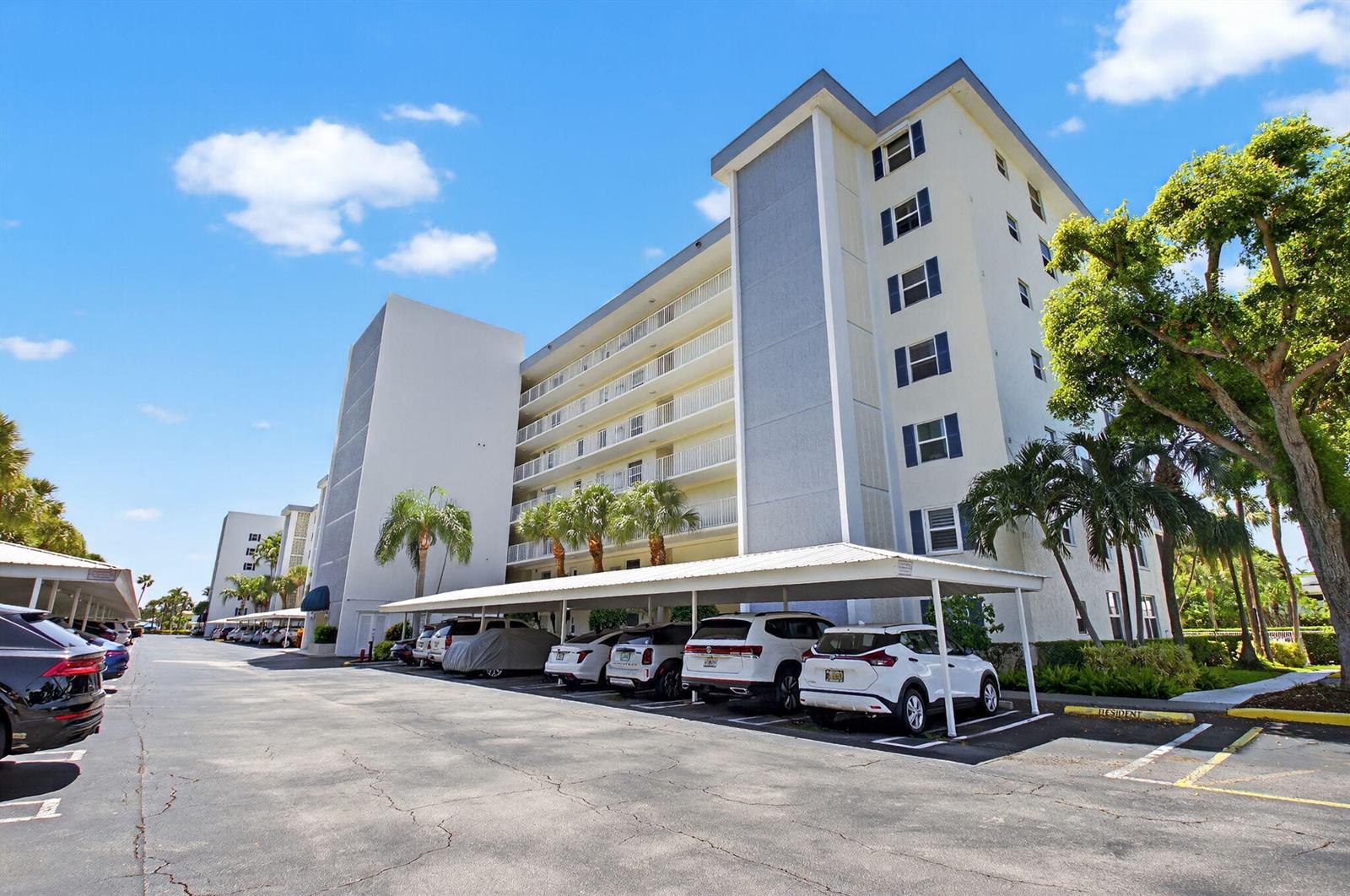 A multi-story apartment building features a covered parking area with several cars parked underneath — 1 Harbourside Drive # 4205, Delray Beach FL 33483, DELRAY BEACH, FL