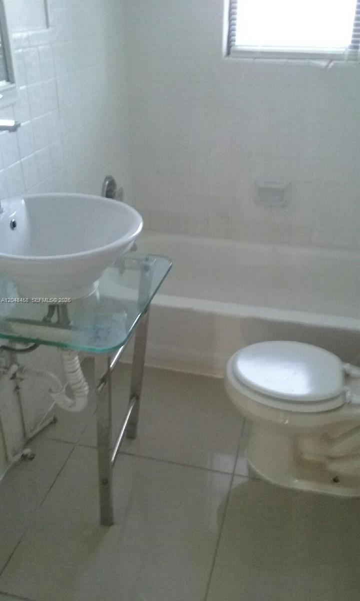 A bathroom features a glass-topped pedestal sink, a white toilet, and a tiled bathtub — NORTH MIAMI BEACH, FL