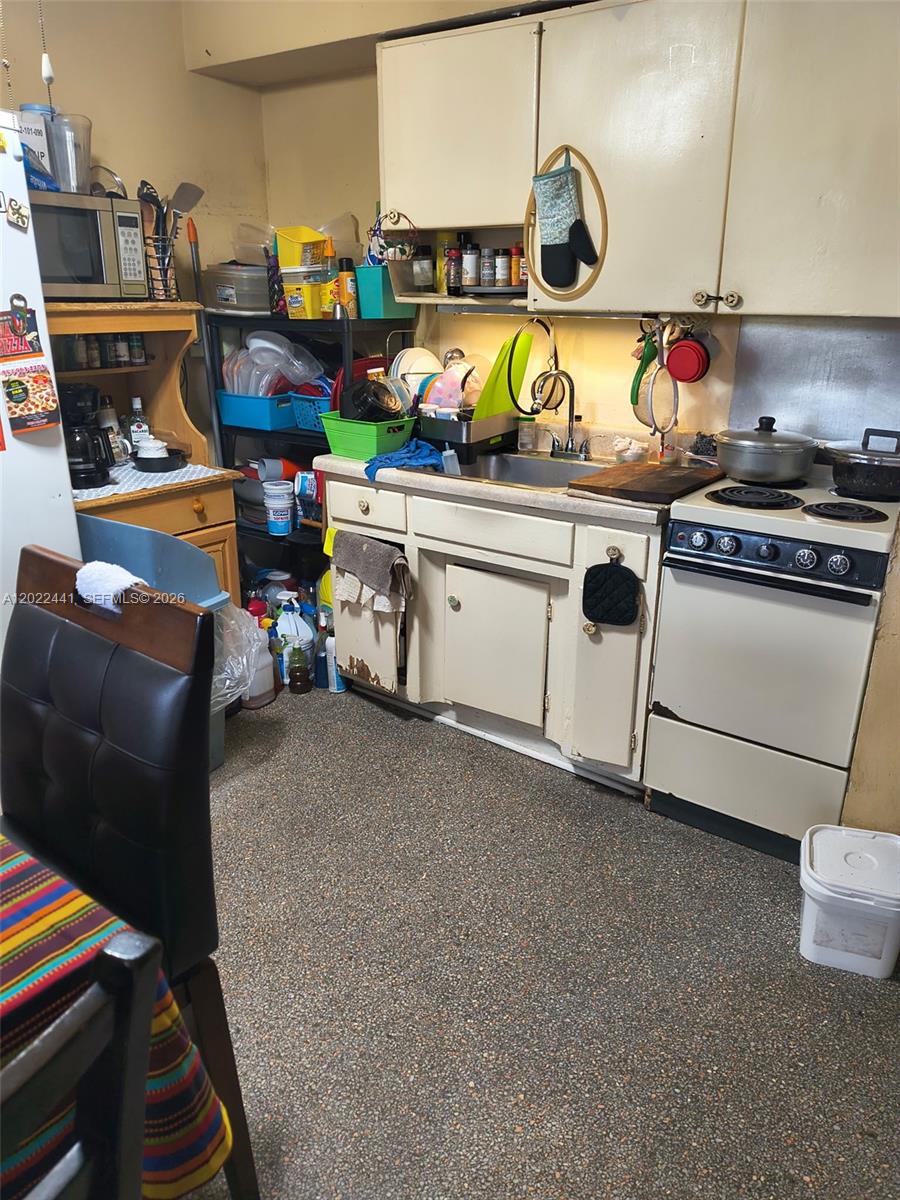 A small kitchen features off-white cabinets, a stainless steel sink, and a white electric stove — 6316 Pierce St, Hollywood FL 33024, HOLLYWOOD, FL