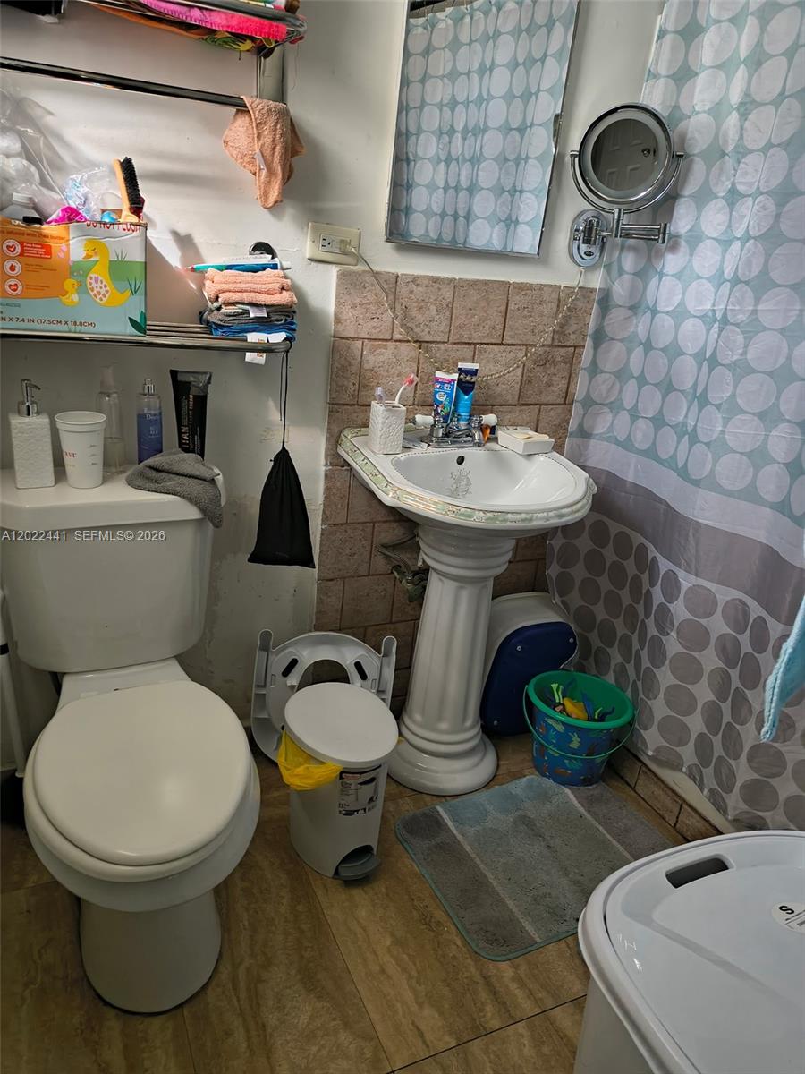 A bathroom features a pedestal sink, a toilet, a shower curtain, and wall-mounted shelving — 6316 Pierce St, Hollywood FL 33024, HOLLYWOOD, FL