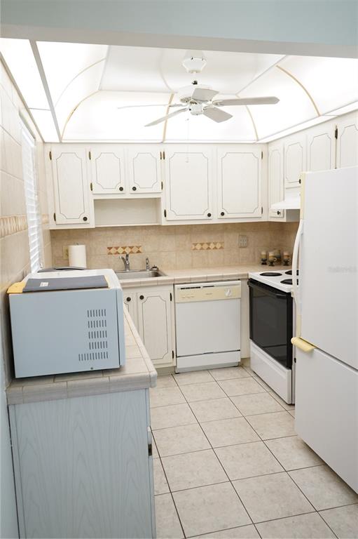 A kitchen features white cabinets, tile countertops, a ceiling fan, and white appliances — 101 CAMBRIDGE TRL UNIT 205, SUN CITY CENTER, FL