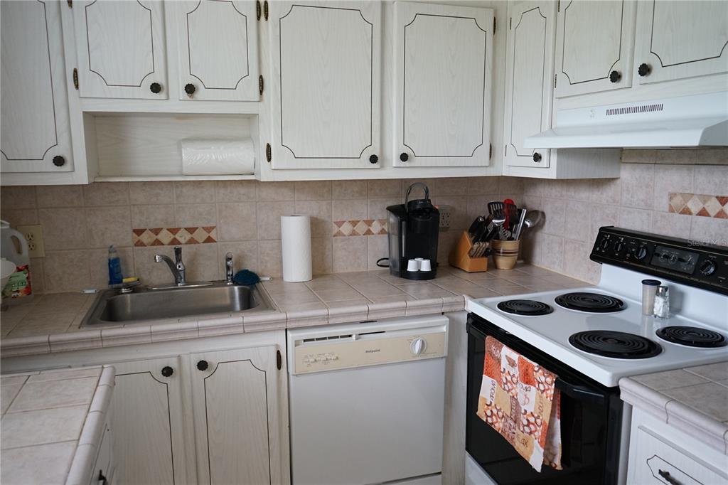 A kitchen features white cabinets, tiled countertops, a stainless steel sink, and a white stove — 101 CAMBRIDGE TRL UNIT 205, SUN CITY CENTER, FL