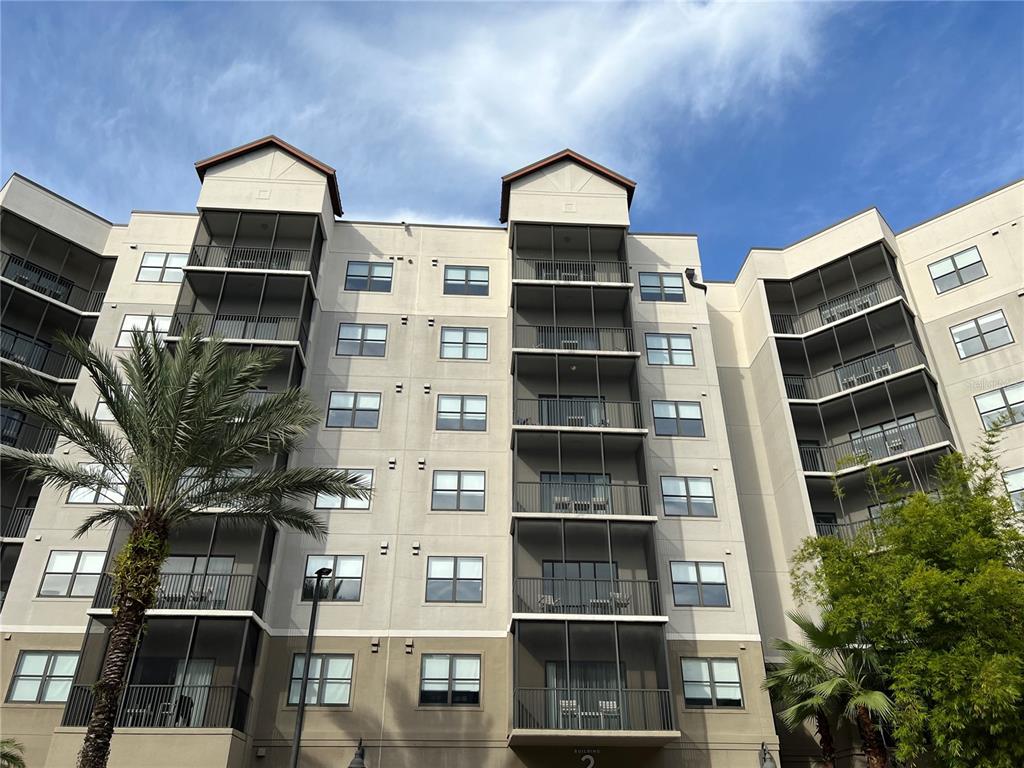 A low-angle exterior view of a multi-story apartment building with screened balconies and palm trees — 14501 GROVE RESORT AVENUE UNIT 1637, WINTER GARDEN, FL