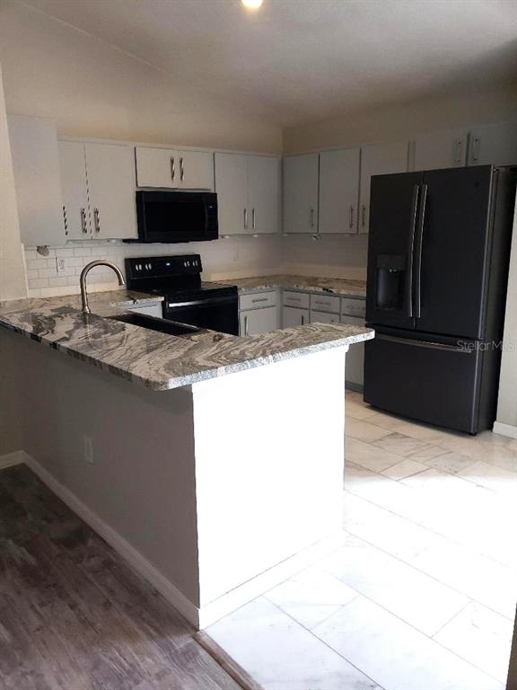 A kitchen features light gray cabinets, granite countertops, a black refrigerator, and a breakfast bar — 4808 LIMERICK DRIVE, TAMPA, FL
