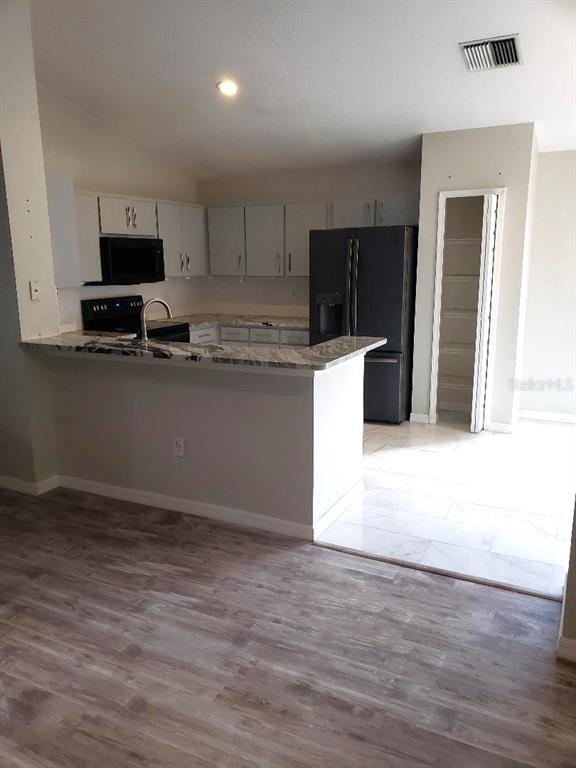 A kitchen features light gray cabinets, granite countertops, a dark refrigerator, and wood-look flooring — 4808 LIMERICK DRIVE, TAMPA, FL