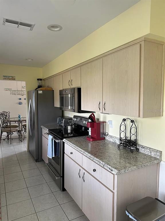 A kitchen features light wood cabinets, granite countertops, stainless steel appliances, and tile flooring — 17808 SE 107TH TERRACE, SUMMERFIELD, FL
