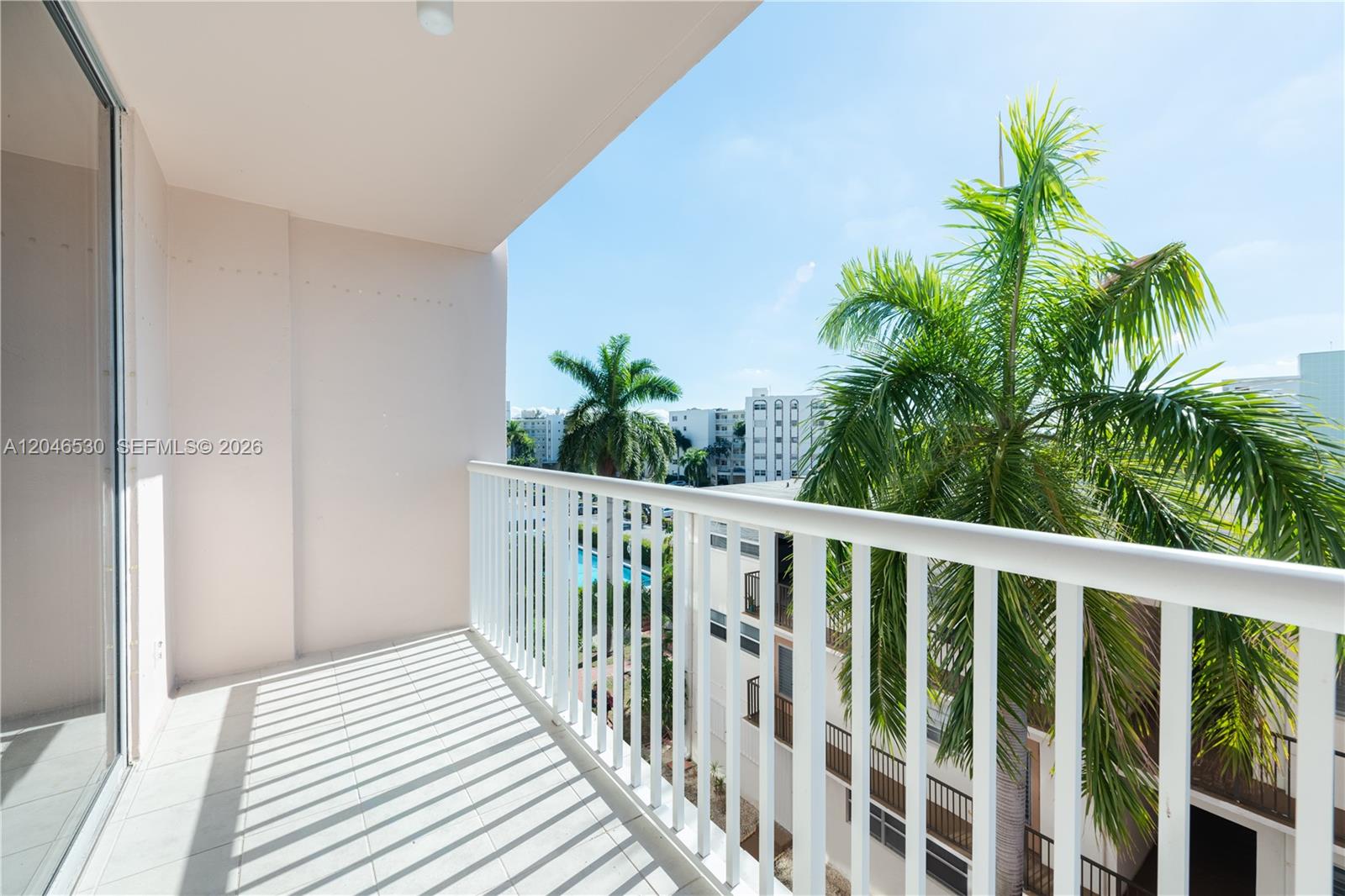 A balcony with white railings overlooks a palm tree and nearby apartment buildings — 3161 S Ocean Dr # 407, Hallandale Beach FL 33009, HALLANDALE BEACH, FL