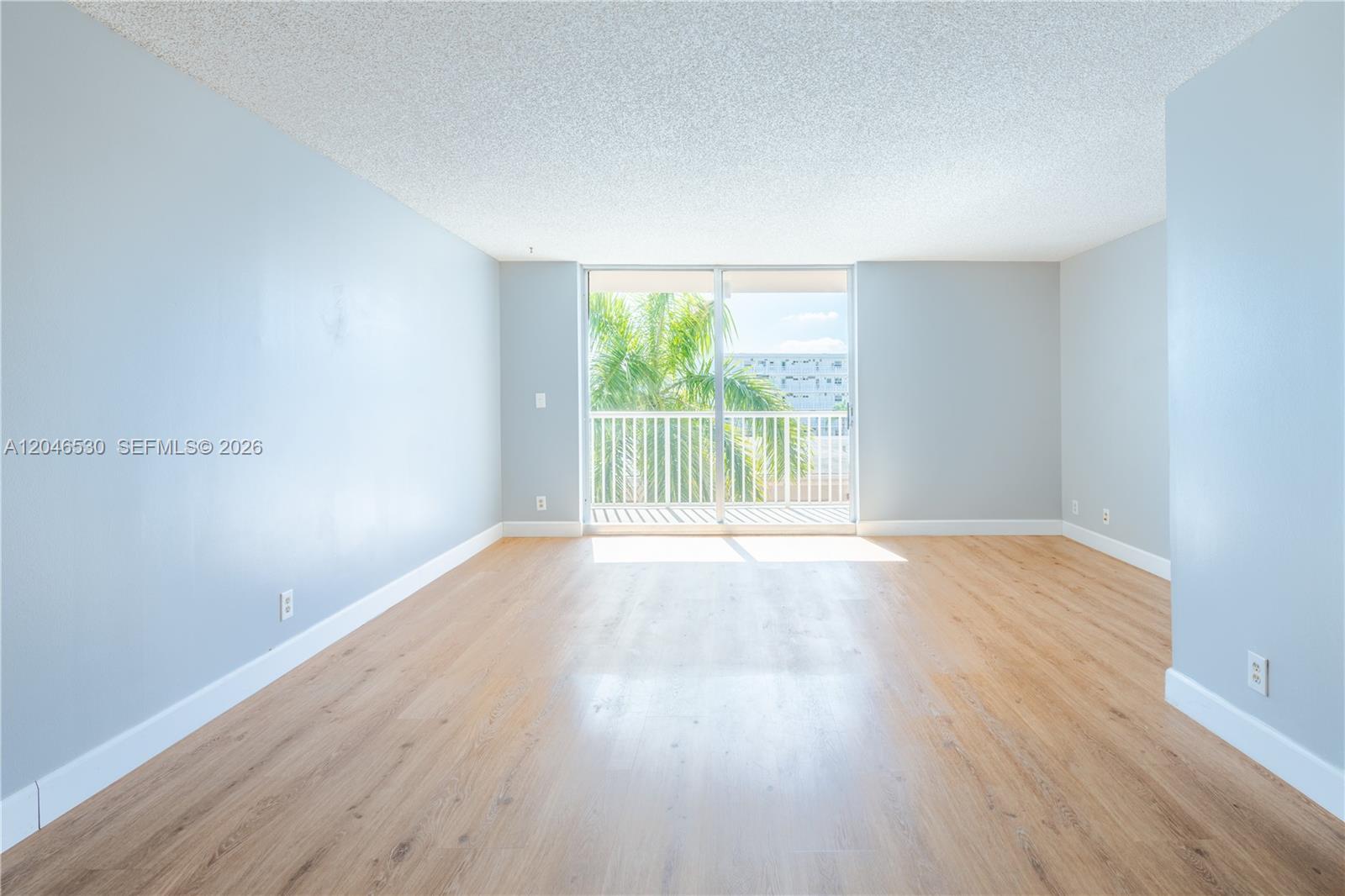 An empty room features light blue walls, wood-look flooring, and a sliding glass door balcony — 3161 S Ocean Dr # 407, Hallandale Beach FL 33009, HALLANDALE BEACH, FL
