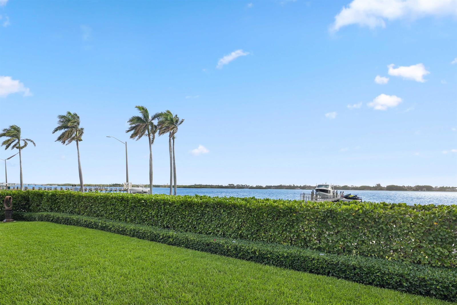 A manicured lawn and hedge overlook a body of water with a boat dock — 5501 S Flagler Drive, West Palm Beach FL 33405, WEST PALM BEACH, FL