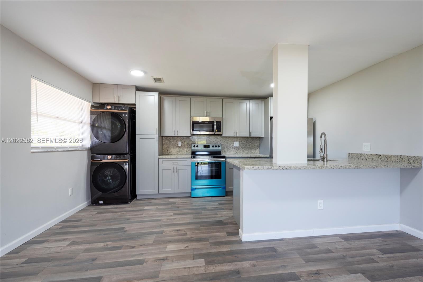 A kitchen features grey cabinets, granite countertops, a stacked washer-dryer unit, and wood-look flooring — 4111 Stirling Rd # 509, Dania Beach FL 33314, DANIA BEACH, FL