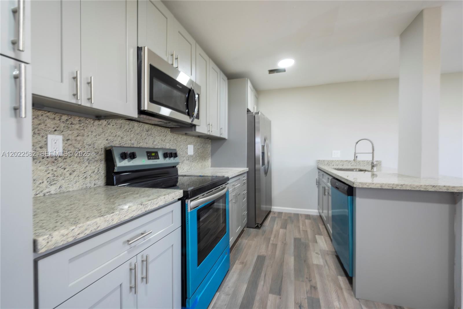 A kitchen features light gray cabinets, granite countertops, stainless steel appliances, and wood-look flooring — 4111 Stirling Rd # 509, Dania Beach FL 33314, DANIA BEACH, FL