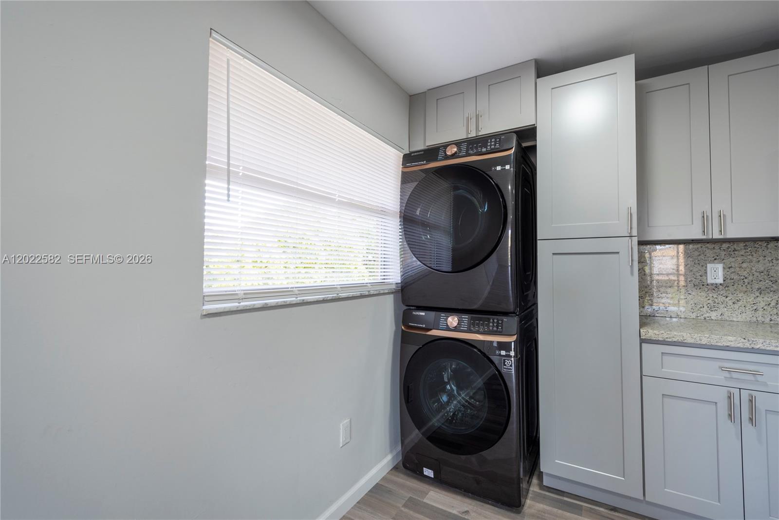 A laundry room features stacked black appliances, grey cabinetry, and a window with blinds — 4111 Stirling Rd # 509, Dania Beach FL 33314, DANIA BEACH, FL