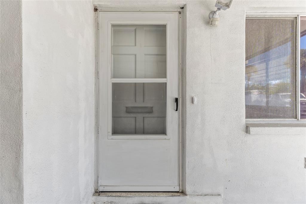 A white storm door with a glass panel is mounted on a textured white exterior wall — 250 NW ROSERY ROAD UNIT 314, LARGO, FL