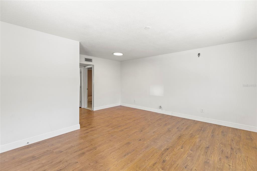 An empty room features white walls, wood-look flooring, and a doorway leading to another area — 250 NW ROSERY ROAD UNIT 314, LARGO, FL