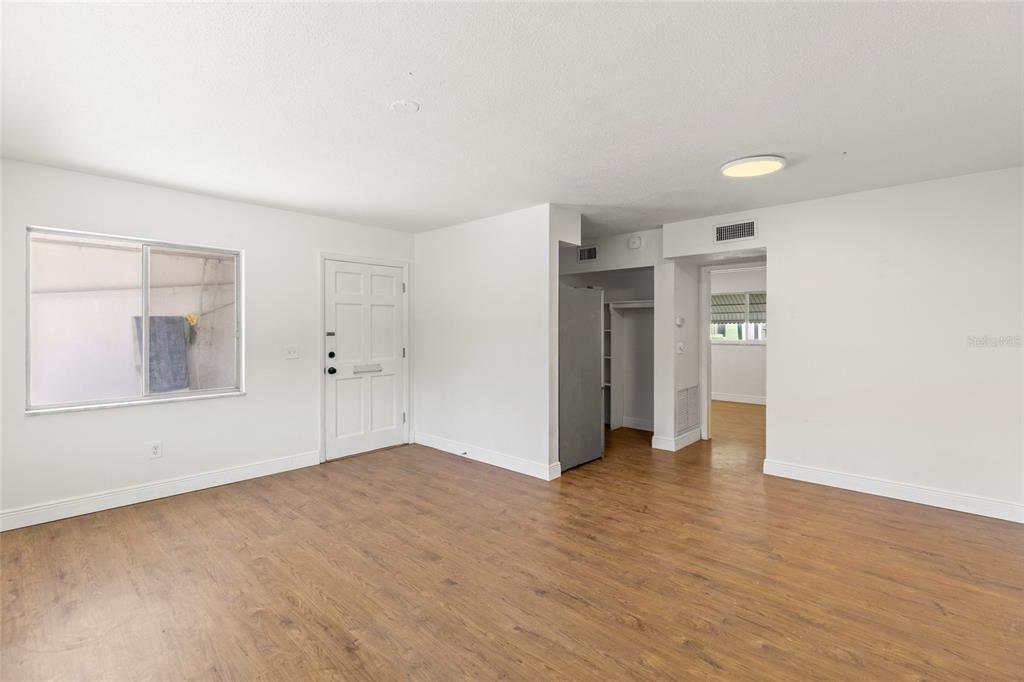 An empty room with white walls, wood-look flooring, a front door, and a kitchen doorway — 250 NW ROSERY ROAD UNIT 314, LARGO, FL