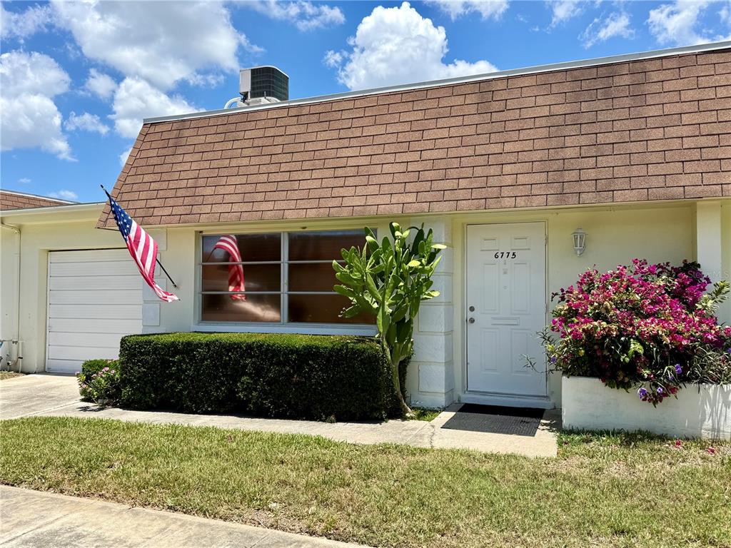 A single-story home exterior features a brown shingled roof, white siding, and a front garden — 6775 ARMAND PLACE N UNIT 4, PINELLAS PARK, FL