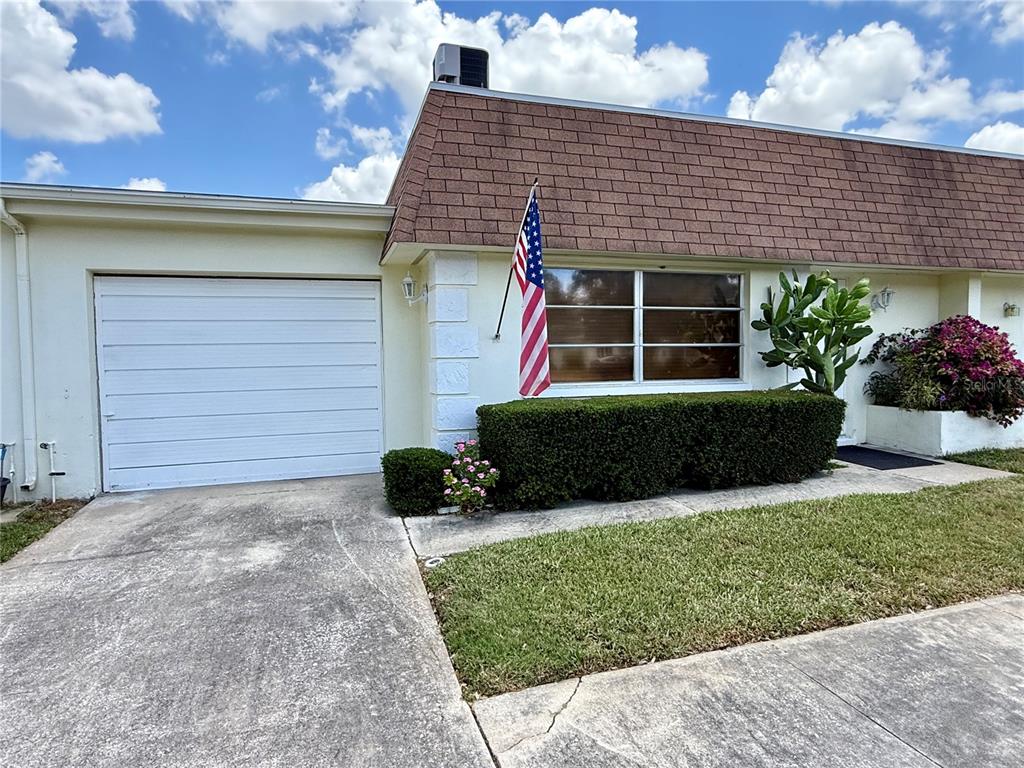 A single-story house with a white garage, brown shingled roof, and an American flag — 6775 ARMAND PLACE N UNIT 4, PINELLAS PARK, FL