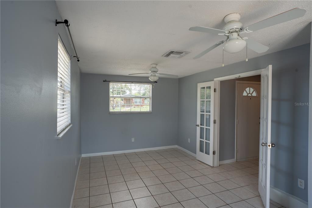 An empty room with light blue walls, tiled floors, two ceiling fans, and French doors — 711 MASON STREET, BRANDON, FL