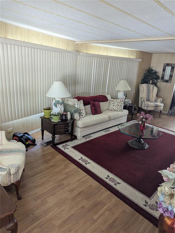 A living room features wood-look flooring, vertical blinds, a sofa, and a large area rug — 34214 CANAL DRIVE N, PINELLAS PARK, FL