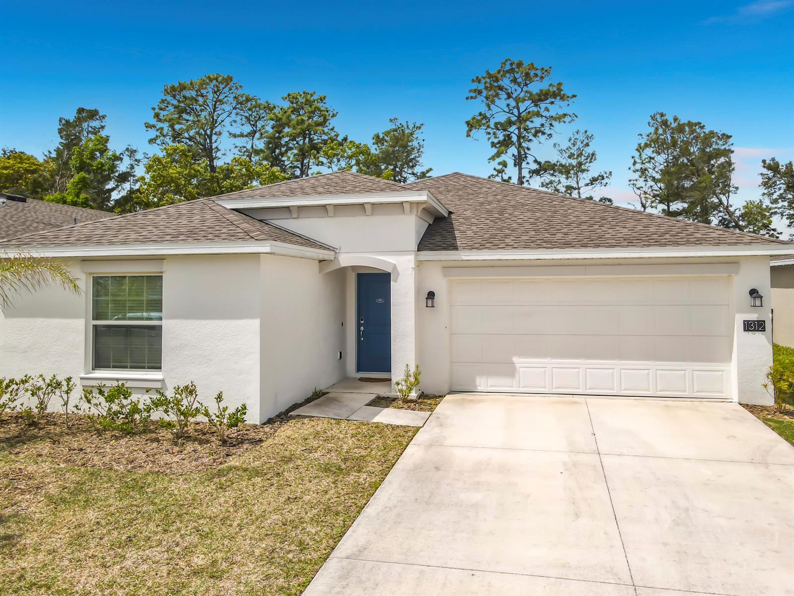 A single-story house with a white stucco exterior, blue front door, and a two-car garage — 1312 Peach Creek Drive, FL 32764, FL