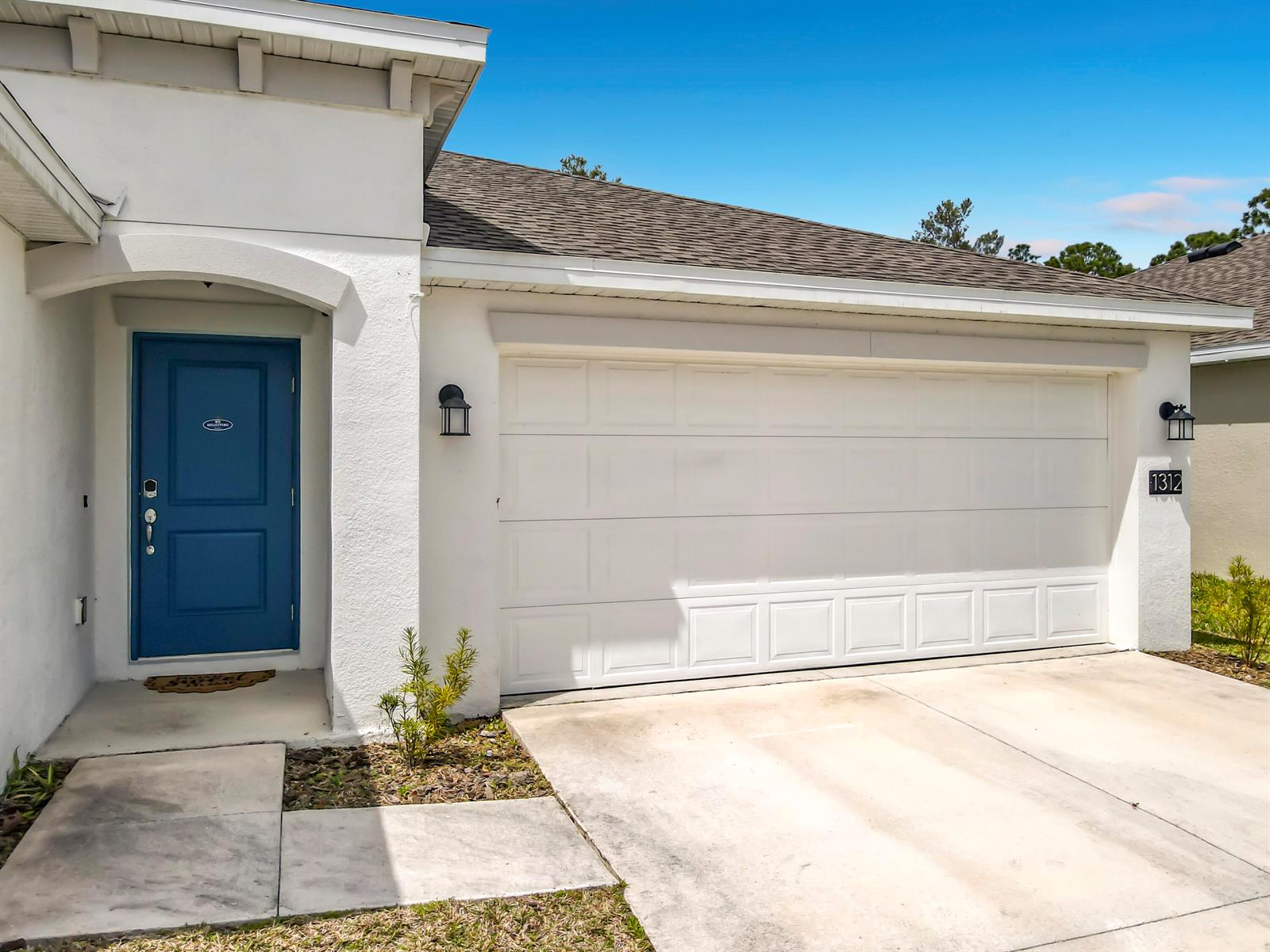 A white house exterior features a blue front door and a two-car garage — 1312 Peach Creek Drive, FL 32764, FL