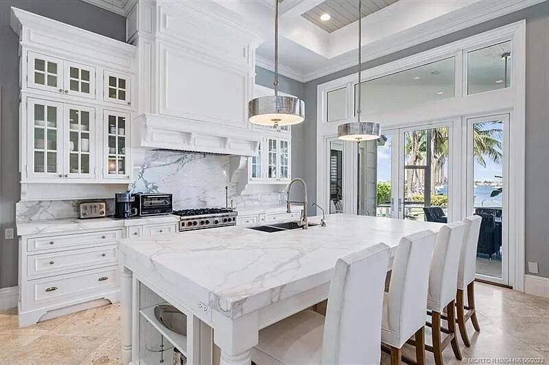 A white kitchen features a large marble island, custom cabinetry, and views of the water — 2941 Lake Drive, Singer Island FL 33404, SINGER ISLAND, FL
