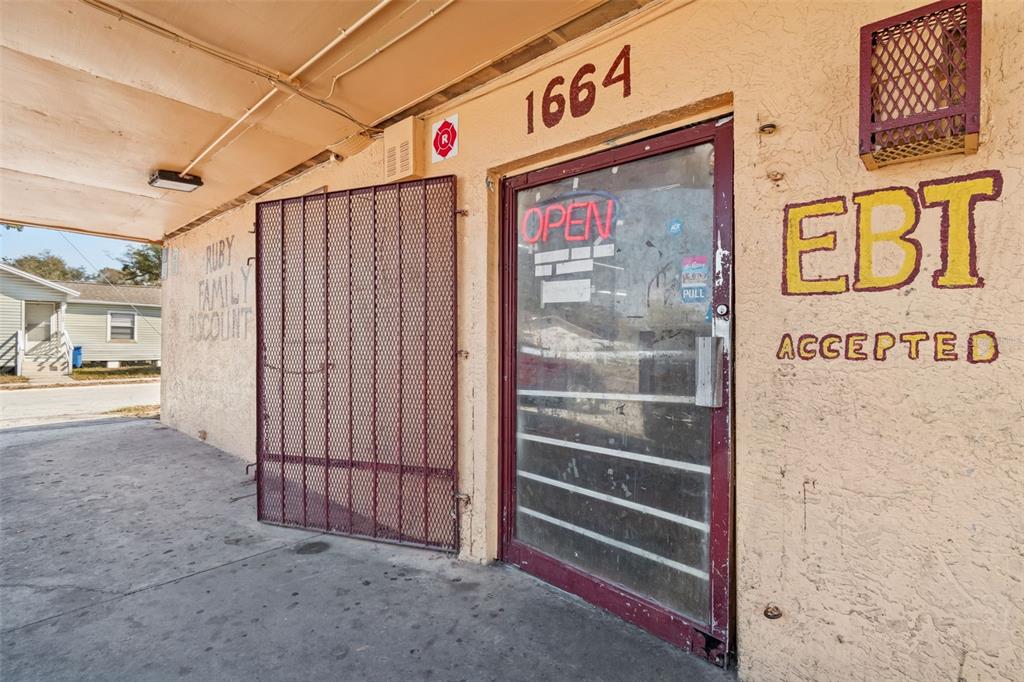 The exterior of a commercial building features a glass door, metal security gate, and signage — 1664 15TH AVENUE S, ST PETERSBURG, FL