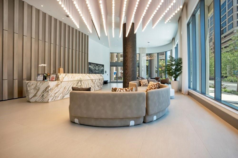 A modern lobby features a marble reception desk, curved seating, and hanging linear light fixtures — 275 1ST AVENUE S UNIT 3808, ST PETERSBURG, FL