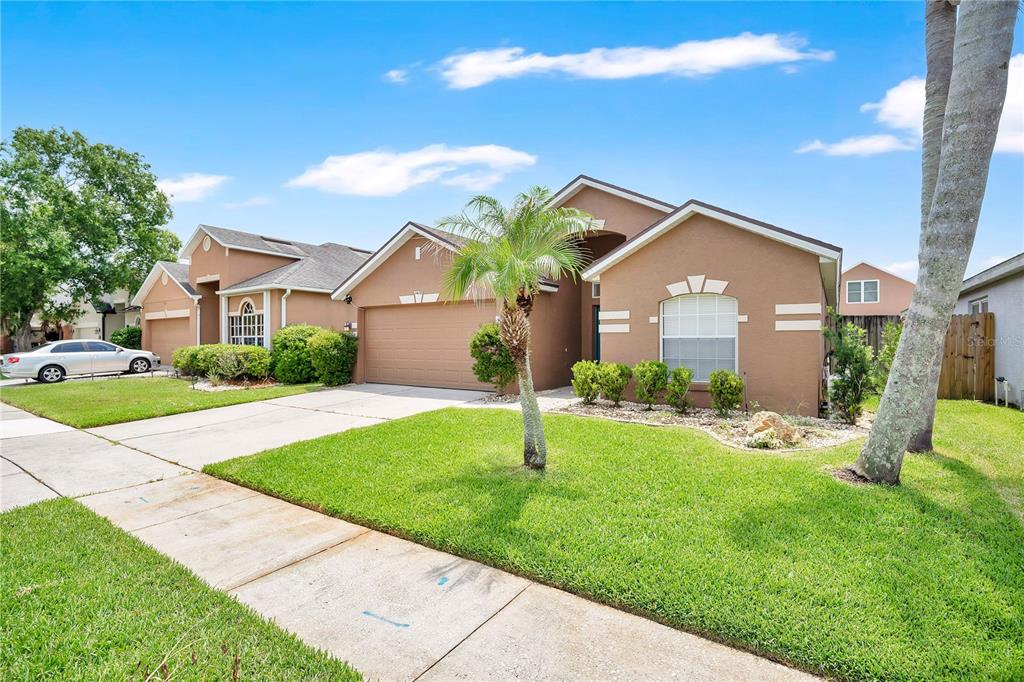 A tan single-story house with a two-car garage, a palm tree, and a green lawn — 14170 SUNRIVER AVENUE, ORLANDO, FL