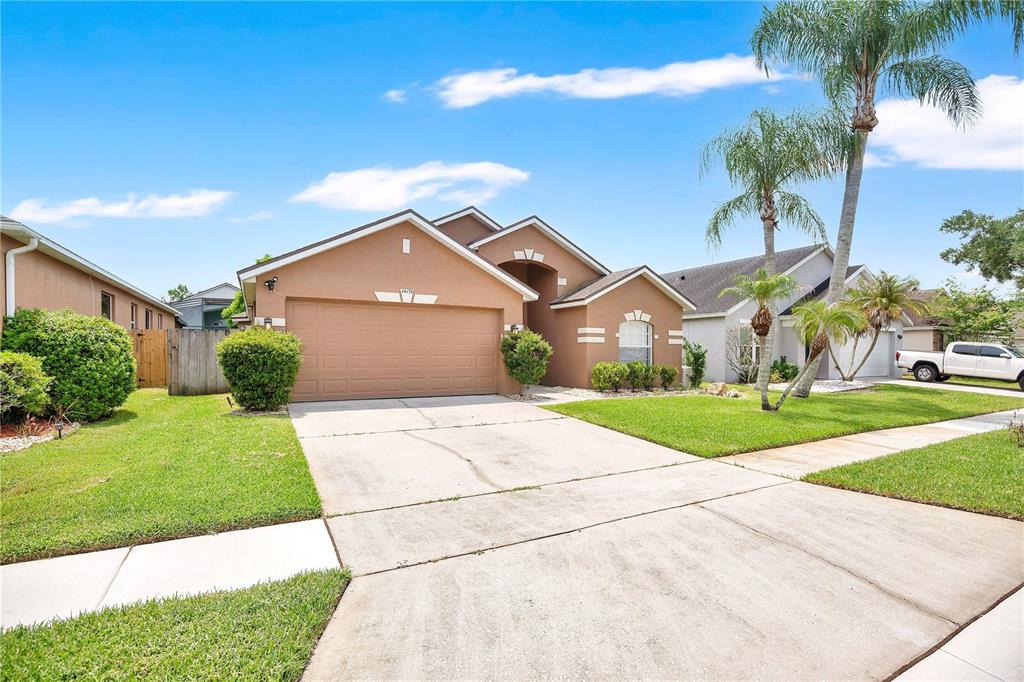 A tan, single-story suburban house with a two-car garage and palm trees in the front — 14170 SUNRIVER AVENUE, ORLANDO, FL