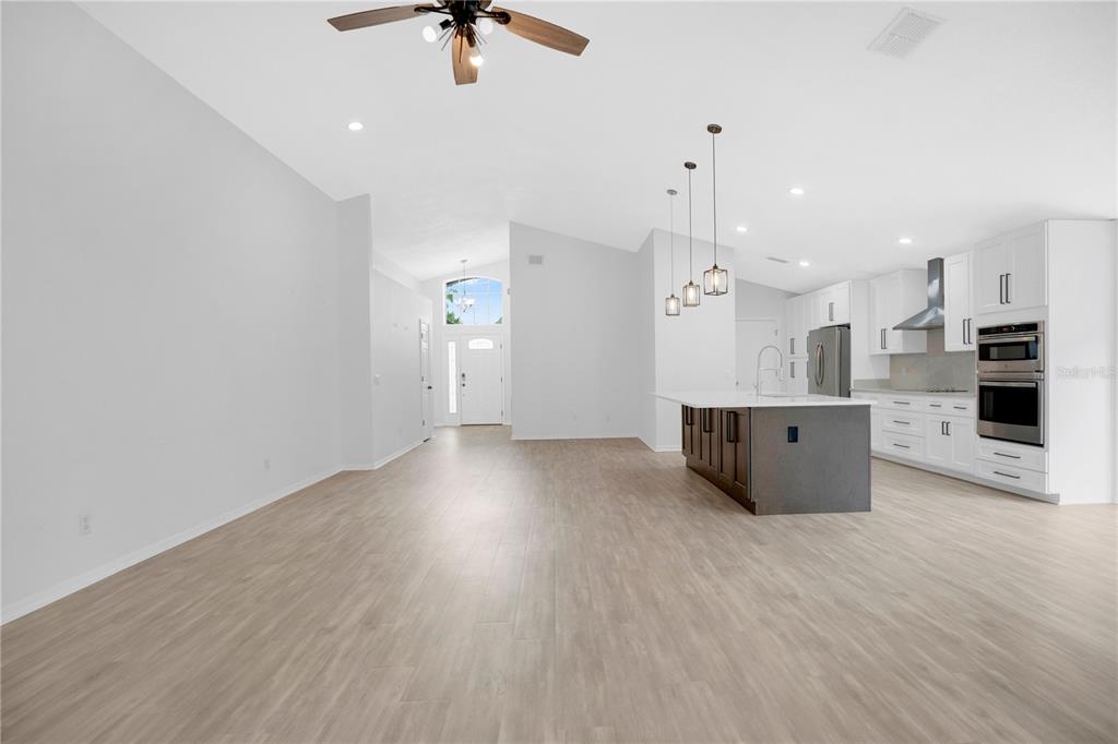 An open-concept kitchen and living area featuring light wood-look flooring and a central island — 14170 SUNRIVER AVENUE, ORLANDO, FL