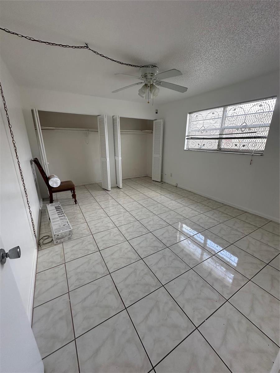 A bedroom with white walls, tiled flooring, a ceiling fan, and two open closets — 348 S Federal Highway # 2, Dania Beach FL 33004, DANIA BEACH, FL