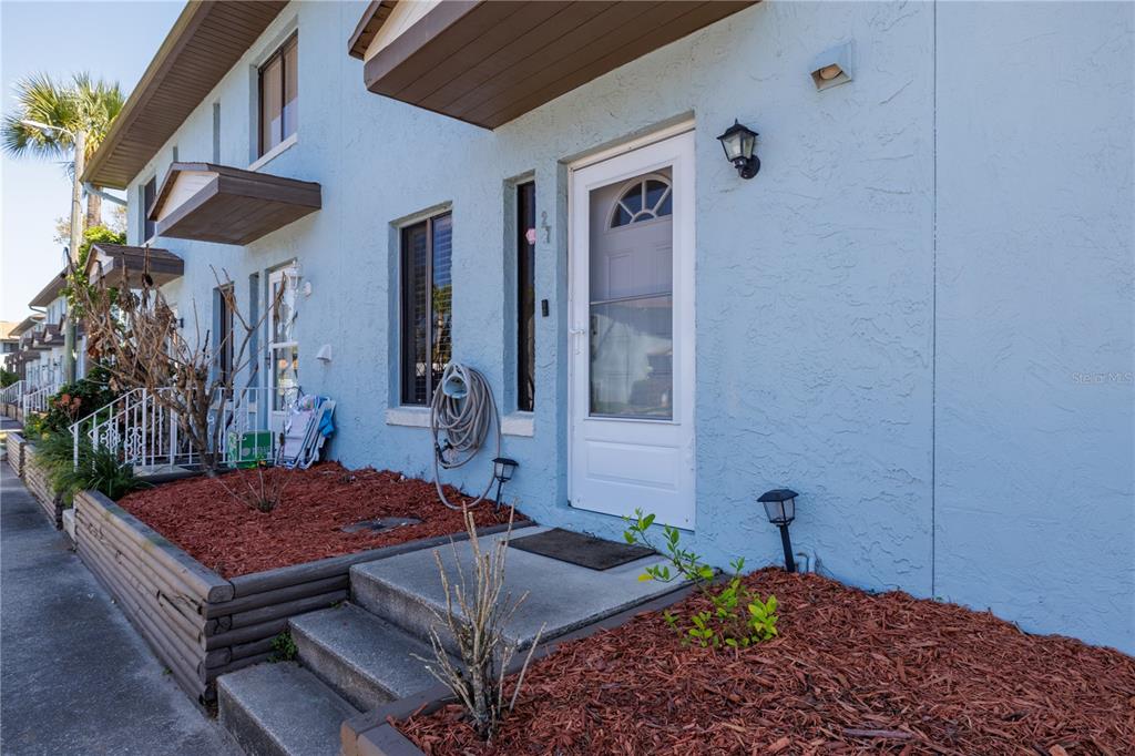 A light blue townhouse exterior features a white front door, concrete steps, and mulch landscaping — 3333 S RIDGEWOOD AVENUE UNIT 27G, PORT ORANGE, FL
