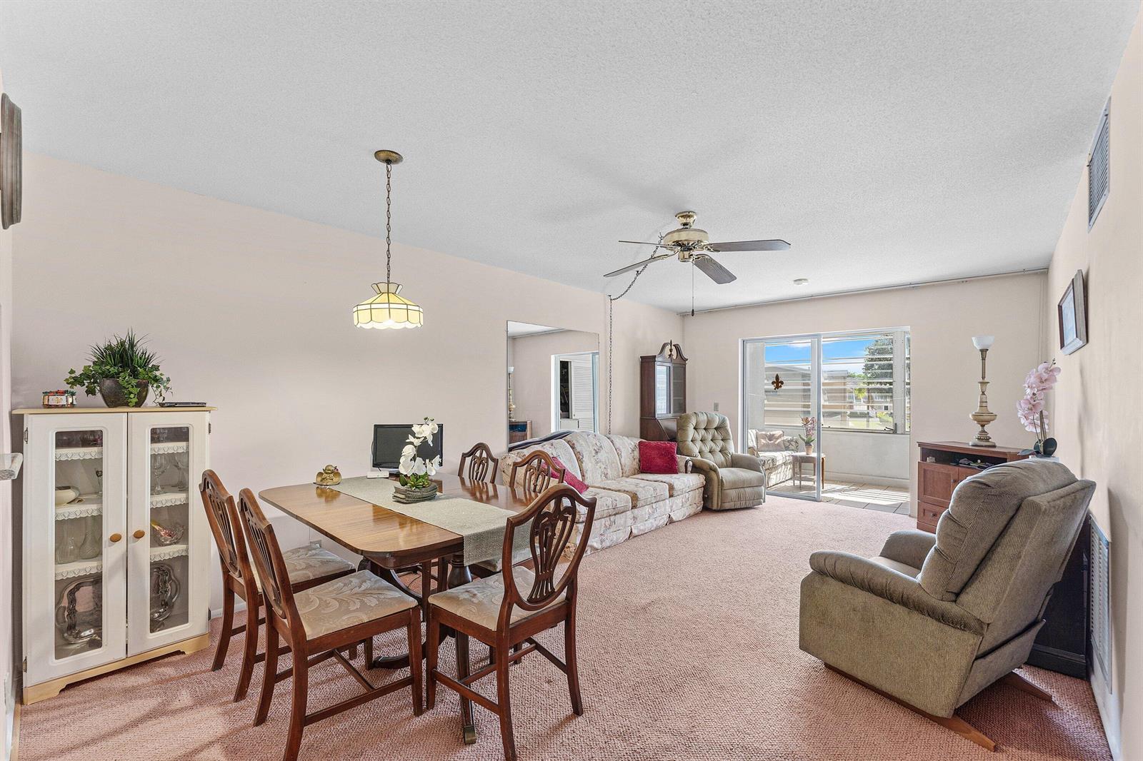A combined dining and living area features pink carpeting, a wooden table, and sliding doors — 2191 NE 1st Court # 202, Boynton Beach FL 33435, BOYNTON BEACH, FL