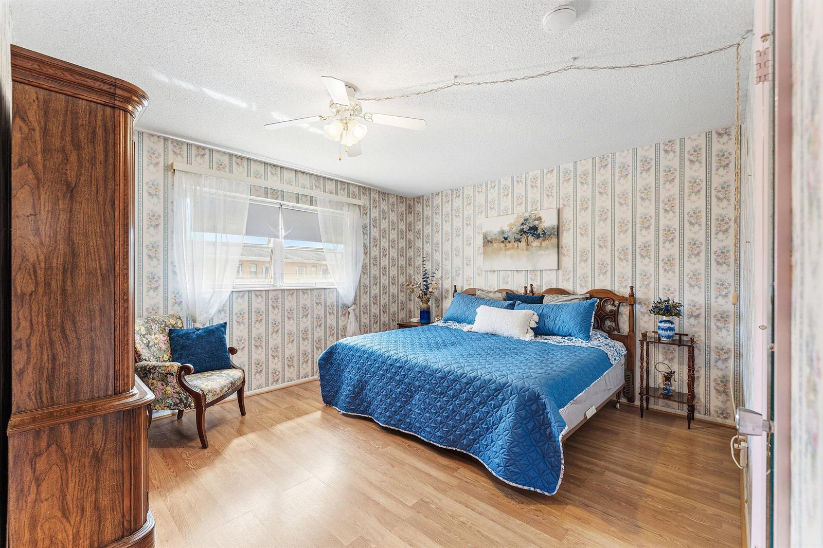 A bedroom features floral wallpaper, a blue quilt on a bed, and light wood flooring — 2191 NE 1st Court # 202, Boynton Beach FL 33435, BOYNTON BEACH, FL