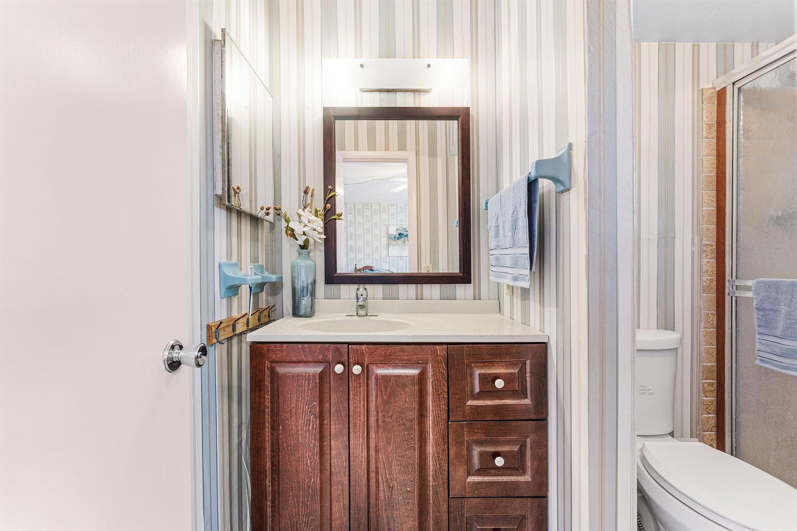 A bathroom features a dark wood vanity, striped wallpaper, a mirror, and a toilet — 2191 NE 1st Court # 202, Boynton Beach FL 33435, BOYNTON BEACH, FL