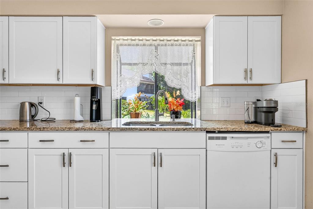 A kitchen features white cabinets, granite countertops, a subway tile backsplash, and a window view — 1846 LAKE CYPRESS DRIVE UNIT 1846, SAFETY HARBOR, FL