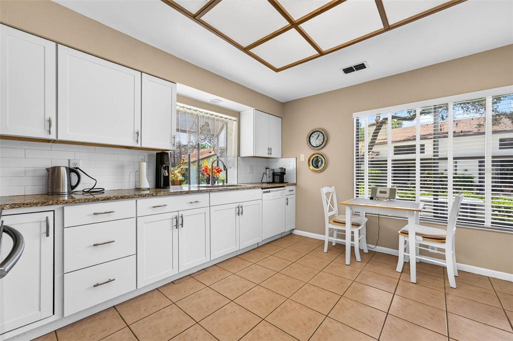 A kitchen features white cabinets, granite countertops, tile flooring, and a small dining area — 1846 LAKE CYPRESS DRIVE UNIT 1846, SAFETY HARBOR, FL