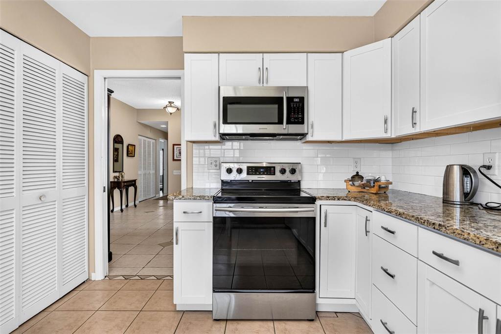A kitchen features white cabinets, stainless steel appliances, granite countertops, and a subway tile backsplash — 1846 LAKE CYPRESS DRIVE UNIT 1846, SAFETY HARBOR, FL