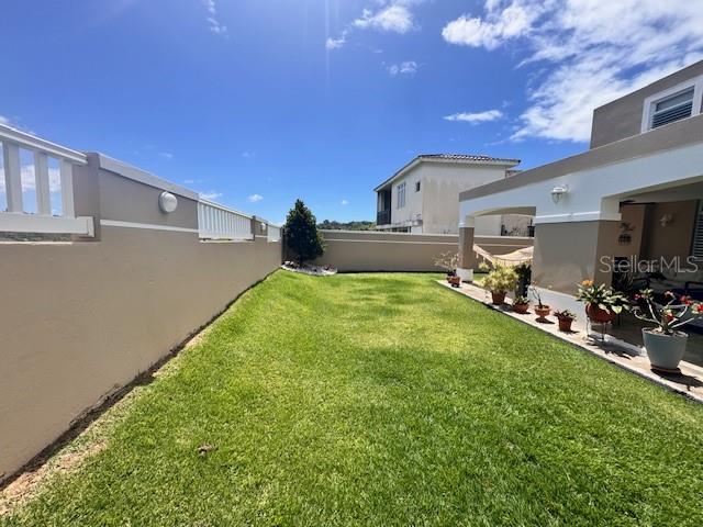 A grassy backyard features a tan wall with white railings and a covered patio area — Camino del Miradero 09, HUMACAO, PR